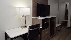 A hotel room with a desk, a chair, a TV, and a wardrobe. - Baymont By Wyndham Batavia - Darien Lake (Elba)