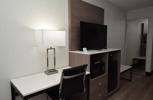 Quarto de hotel com escrivaninha, cadeira, televisão e guarda-roupa.