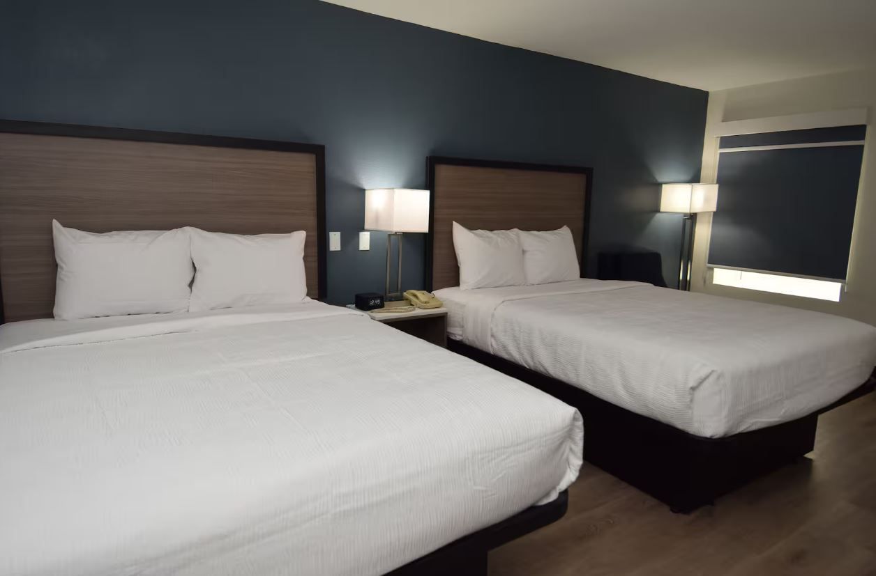 A hotel room with two beds, each with a wooden headboard, white bedding, and bedside lamps.