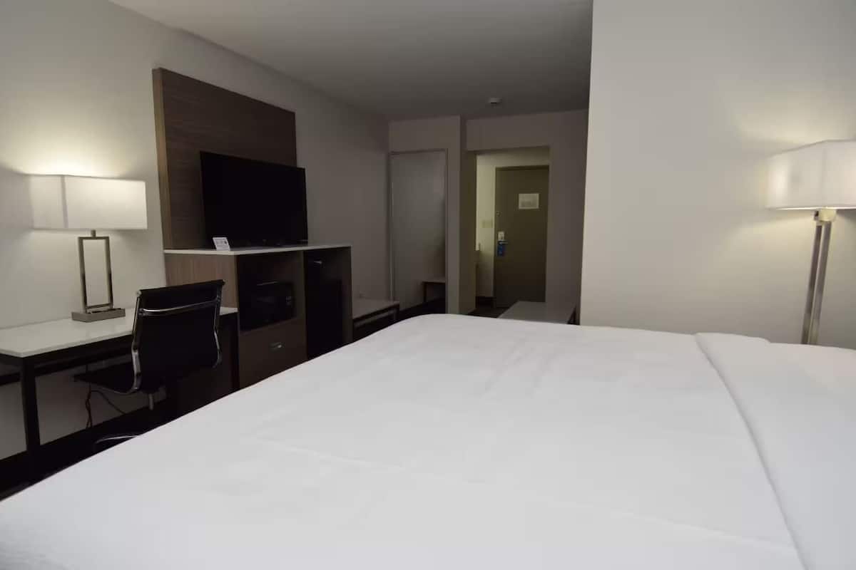 A hotel room with a large bed, a desk with a chair, a television, and a door leading to another room.
