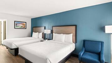 A hotel room with two beds, a blue armchair, and a framed picture on the wall.