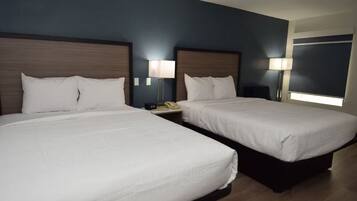 A hotel room with two beds, each with a wooden headboard, white bedding, and bedside lamps.