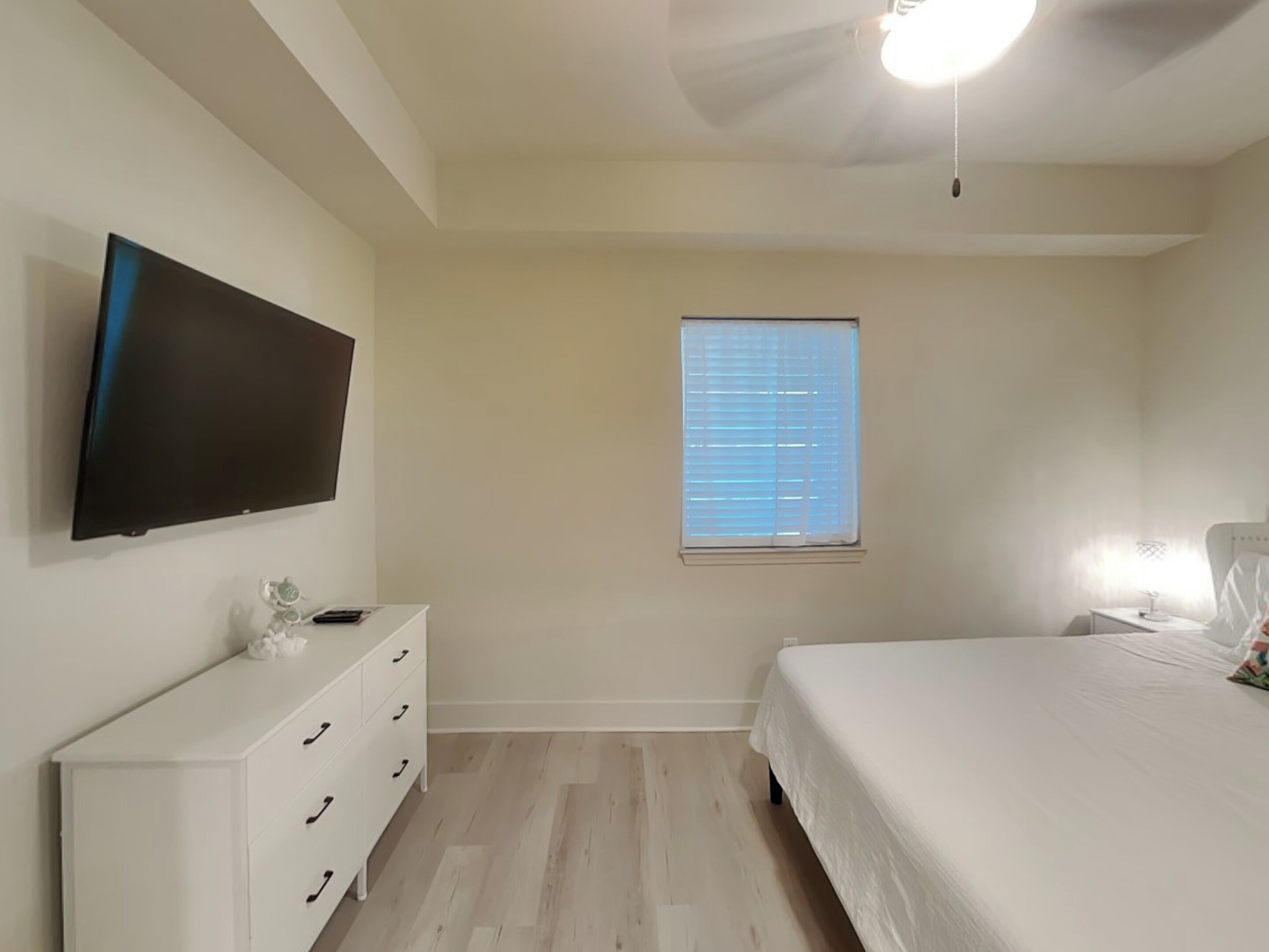 A bedroom with a bed, a dresser, a TV, a window, and a ceiling fan.