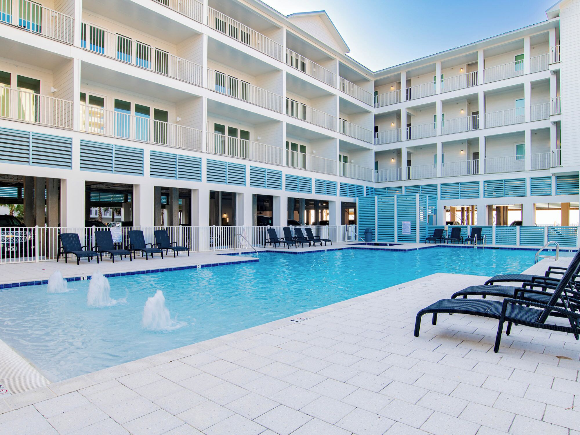 Ein Hotel mit mehreren Etagen, einem zentralen Schwimmbecken, Sitzgelegenheiten im Freien und Balkonen.