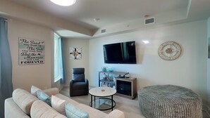 Una sala de estar con sofá, reposapiés, televisor, chimenea y obras de arte en la pared.