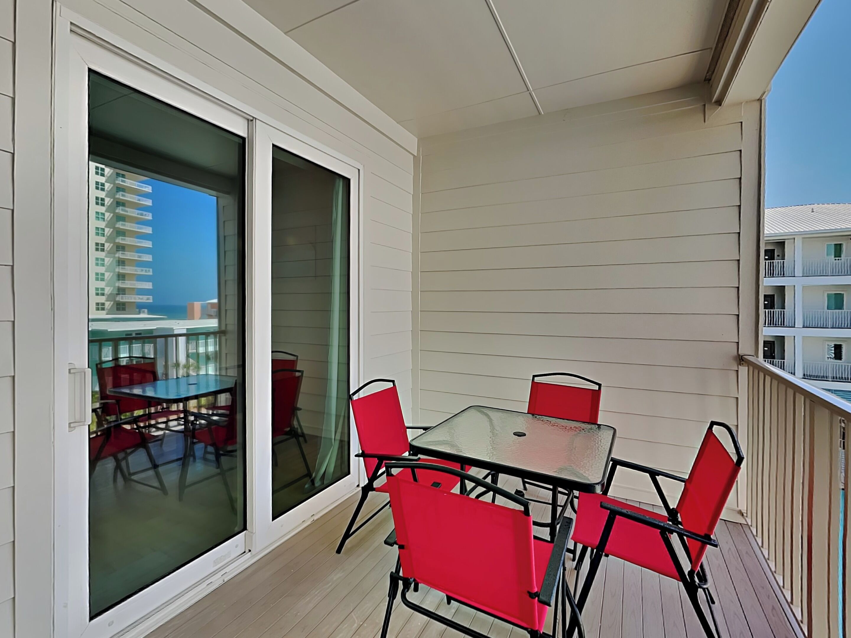 A balcony with a glass door, a table, and red chairs.