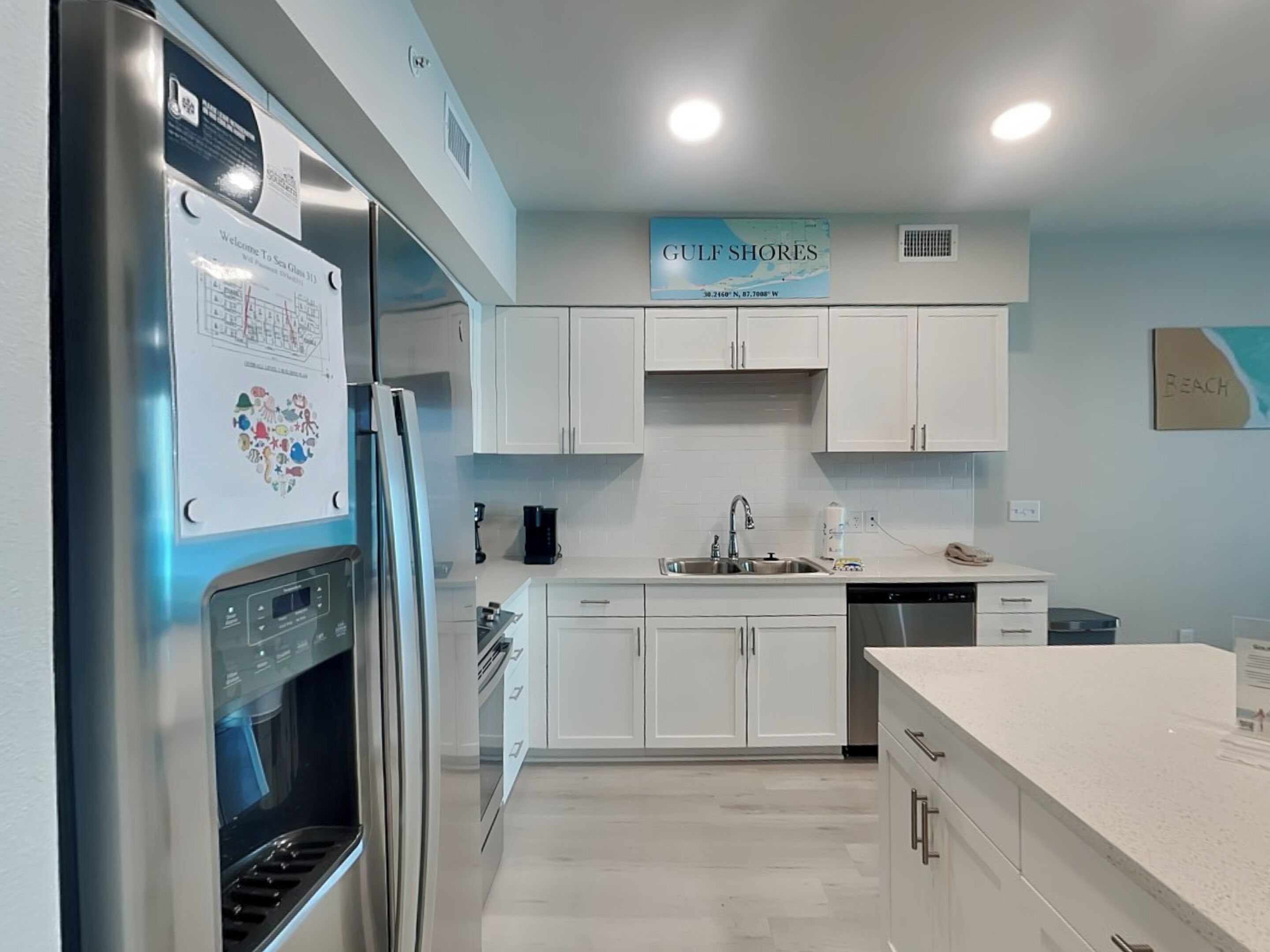 A modern kitchen with white cabinets, stainless steel appliances, and a sign indicating the Gulf Shores location.