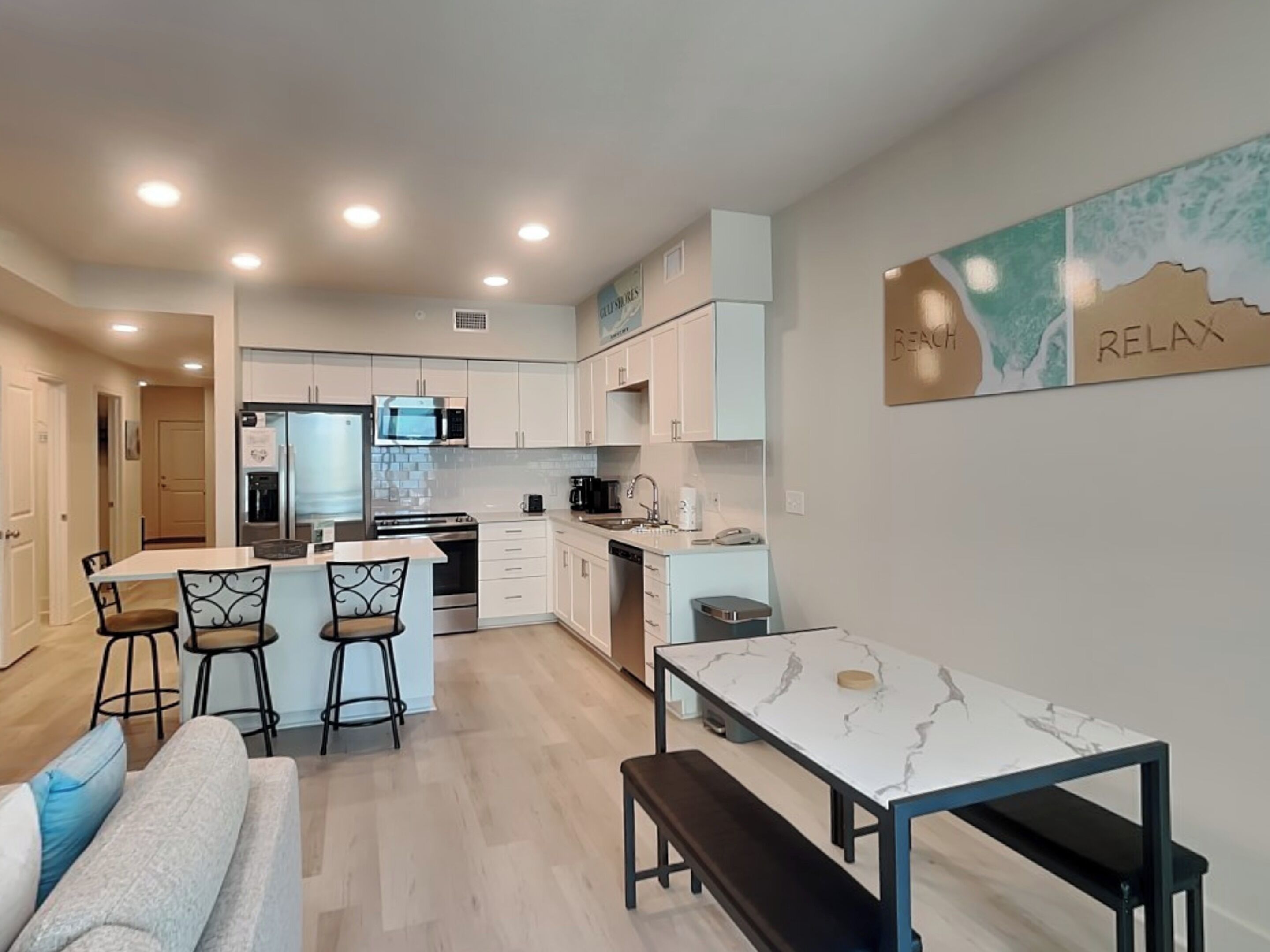 A modern kitchen with white cabinets, a central island, and a dining area with a marble table and bench.