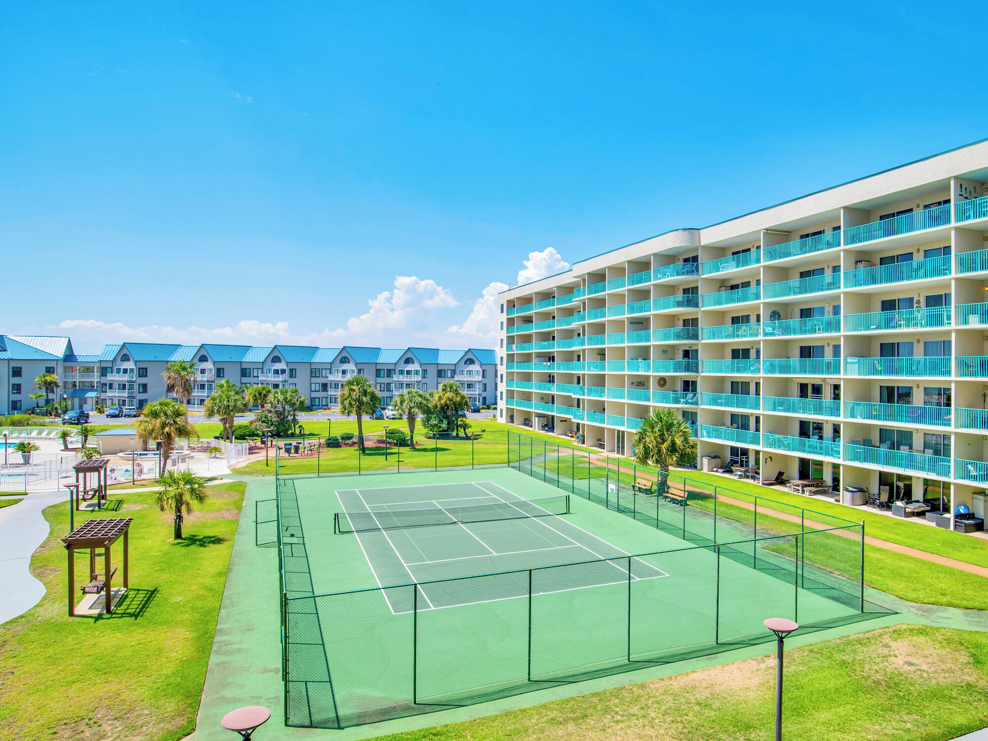 Ein Hotel mit mehreren Balkonen, einem Tennisplatz und einem Poolbereich.