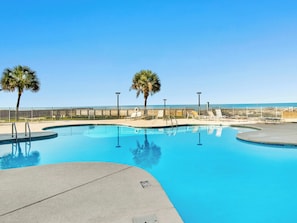 A clear blue pool with a curved edge, surrounded by a low fence, palm trees, and lounge chairs. - Royal Gulf Beach & Racquet Club #5816 by Southern Vacation Rentals (Gulf Shores)