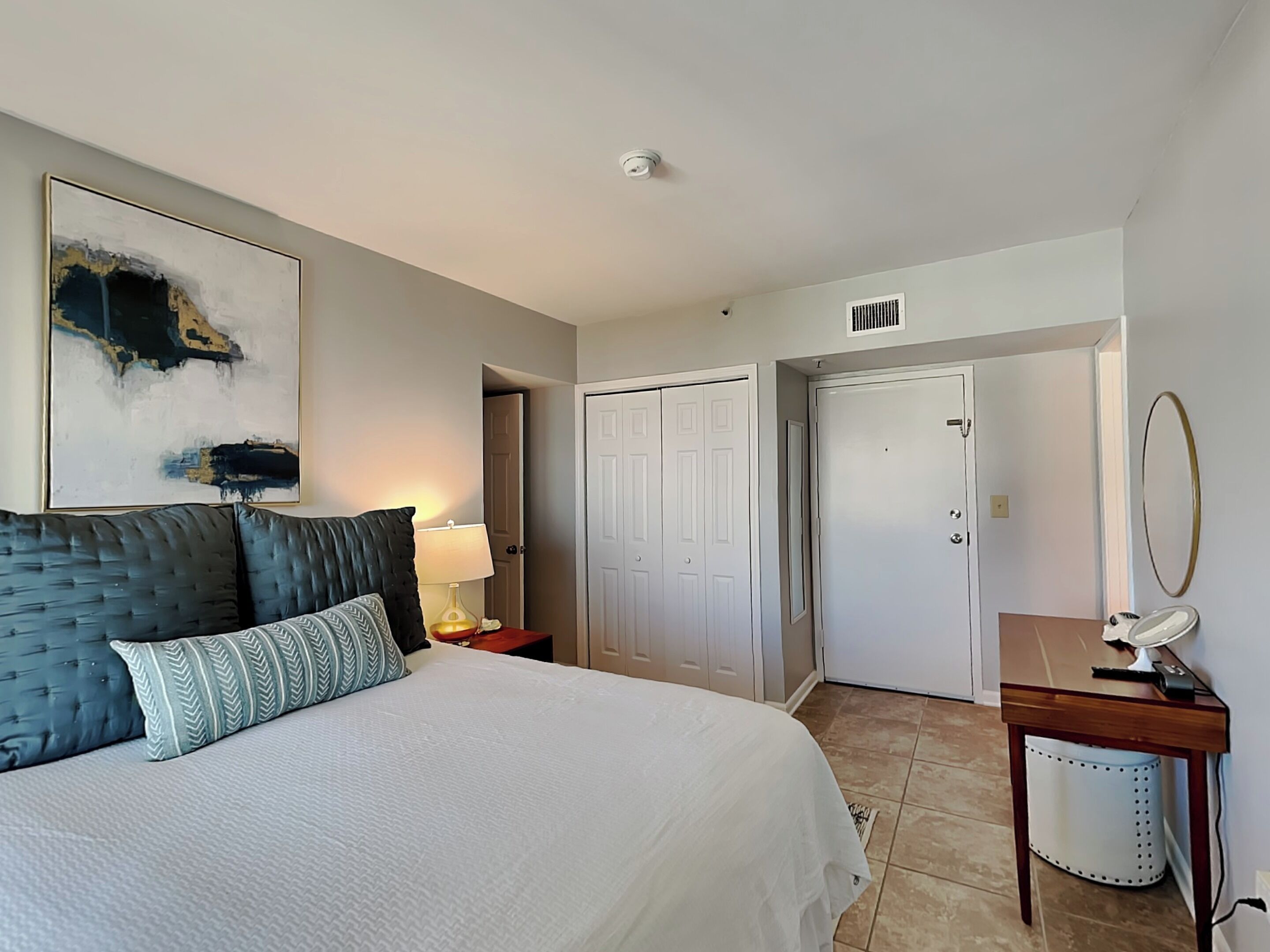 A bedroom with a large bed, a bedside lamp, a wardrobe, and a mirror.