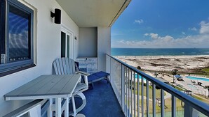 Ein Balkon mit Tisch und Stühlen, der Blick auf einen Strand mit einem Pool freigibt.