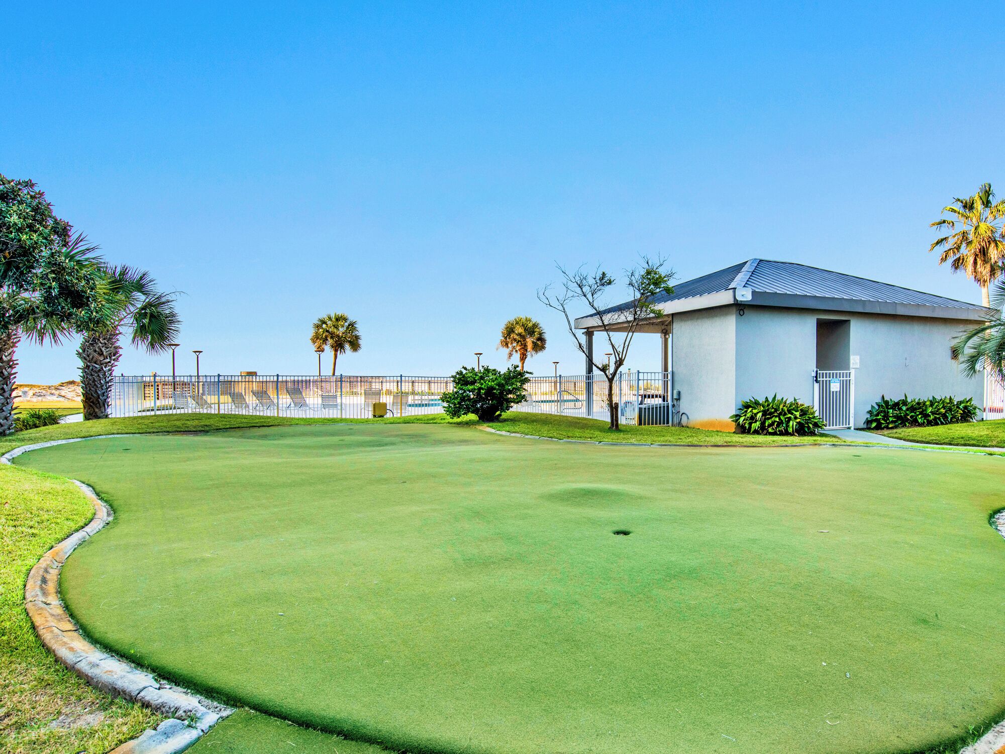 Un parcours de golf doté d’un club-house, de palmiers et surplombant un ciel bleu dégagé.