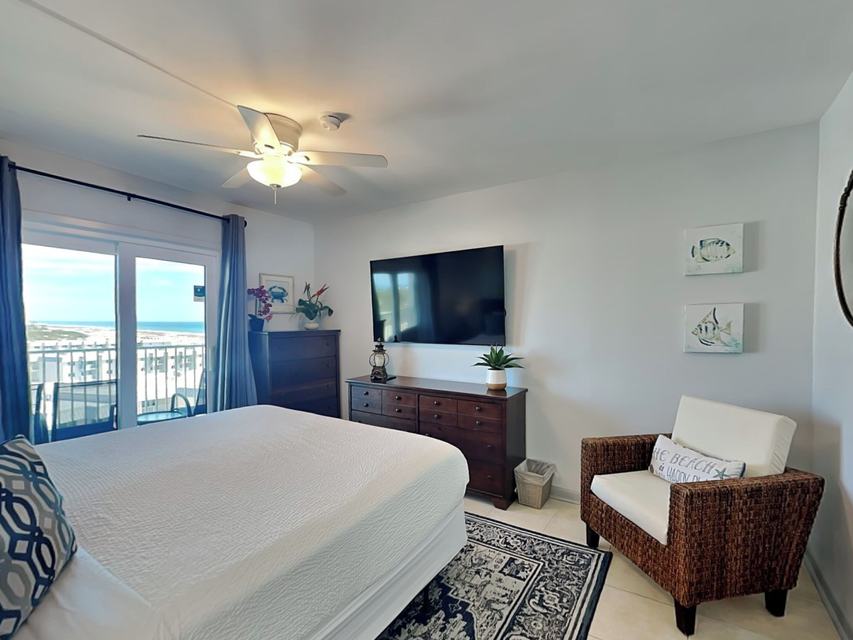 Un dormitorio con cama, cómoda, televisor, una silla y vista a la playa.