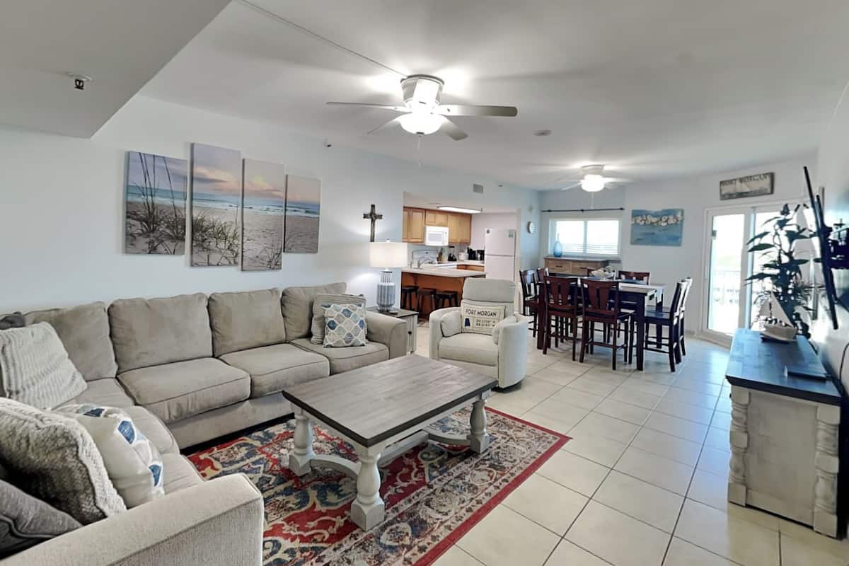 A spacious living room with a large sofa, a coffee table, and a dining area with a kitchen in the background.