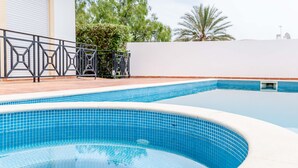 Una piscina con azulejos azules, una cerca de metal y una pared blanca con vegetación al fondo.