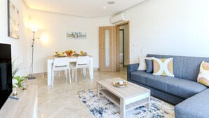 Una sala moderna con un sofá gris, una mesa de centro de madera y una zona de comedor blanca con una mesa y sillas.