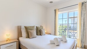 Una cama bien hecha con almohadas y toallas, una lámpara de noche y una ventana con cortinas.