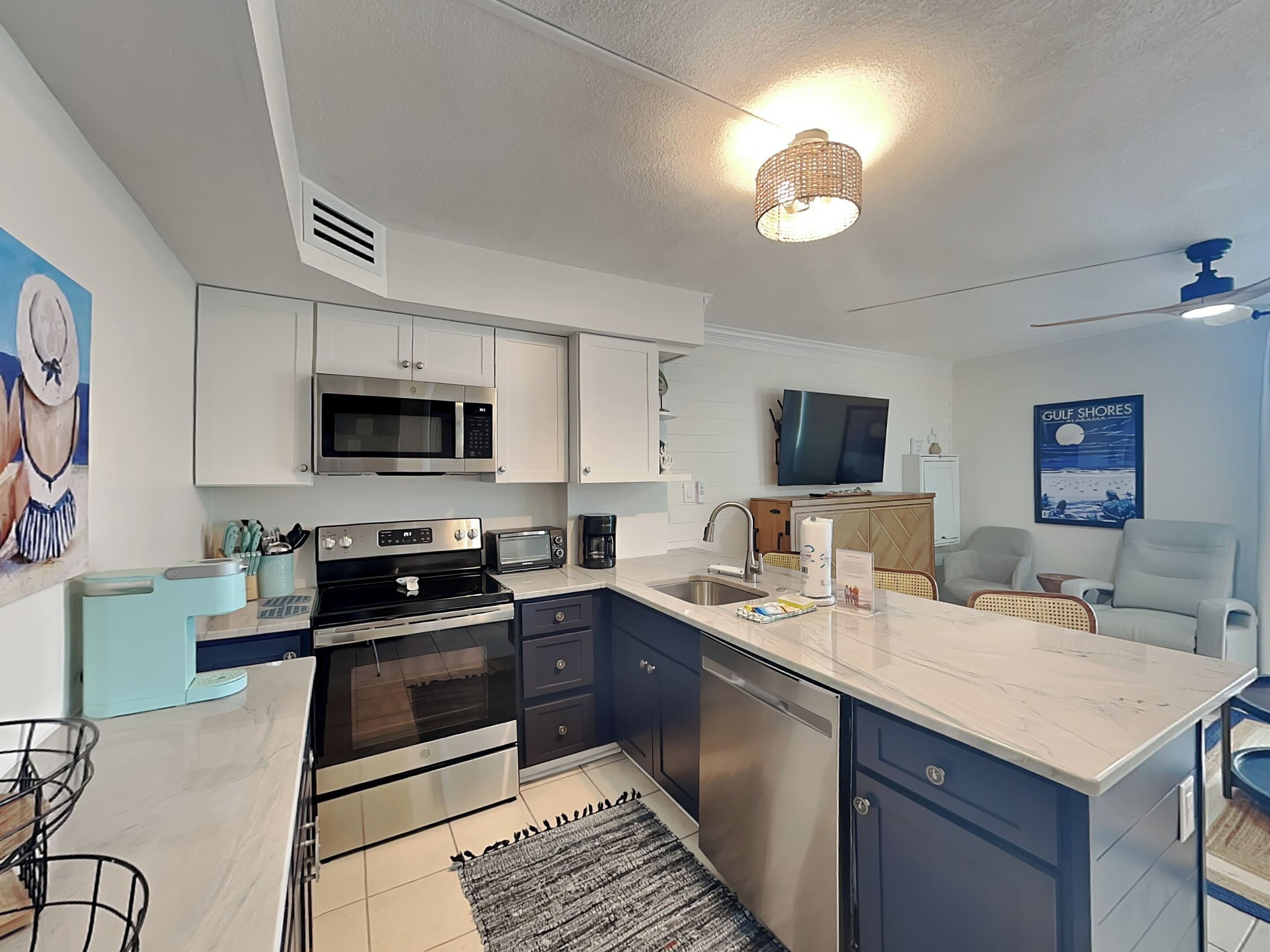 A modern kitchen with a microwave, stove, and dishwasher, a large island with a sink, and a television above the counter.