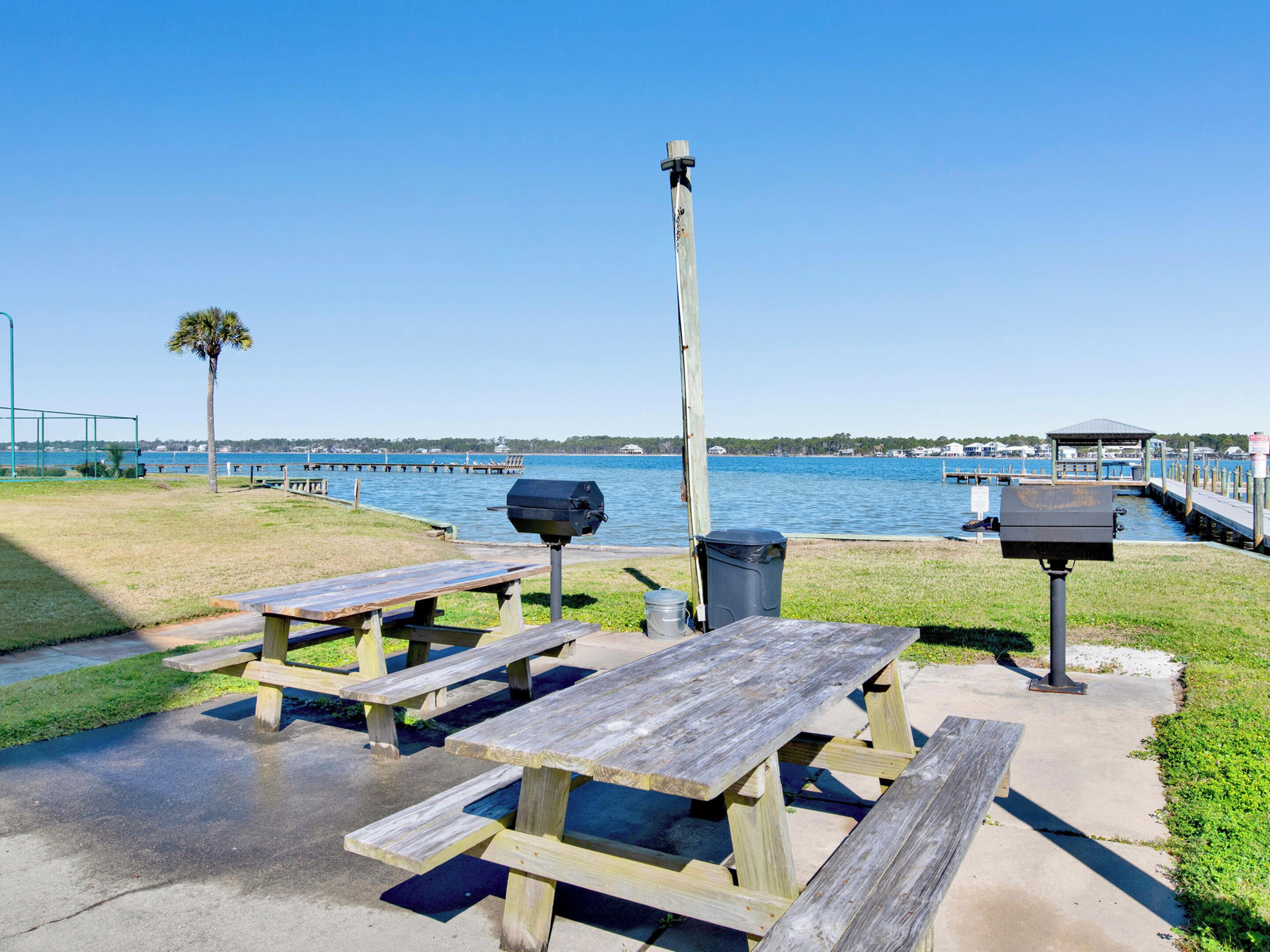 A waterfront picnic area with wooden benches and a grill.