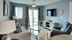 A living room with a ceiling fan, a TV mounted on the wall, and a dining table with chairs. - Gulf Shores Plantation #4206 by Southern Vacation Rentals (Gulf Shores)