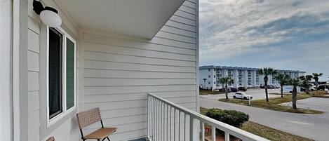 A balcony with wicker furniture, a white railing, and a view of a parking lot and buildings in the background.