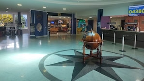 A spacious lobby with a large compass floor design, a coffee shop, and a counter with a phone number sign. - Condominio Golden Dolphin Resort via Roberto Imoveis (Caldas Novas)