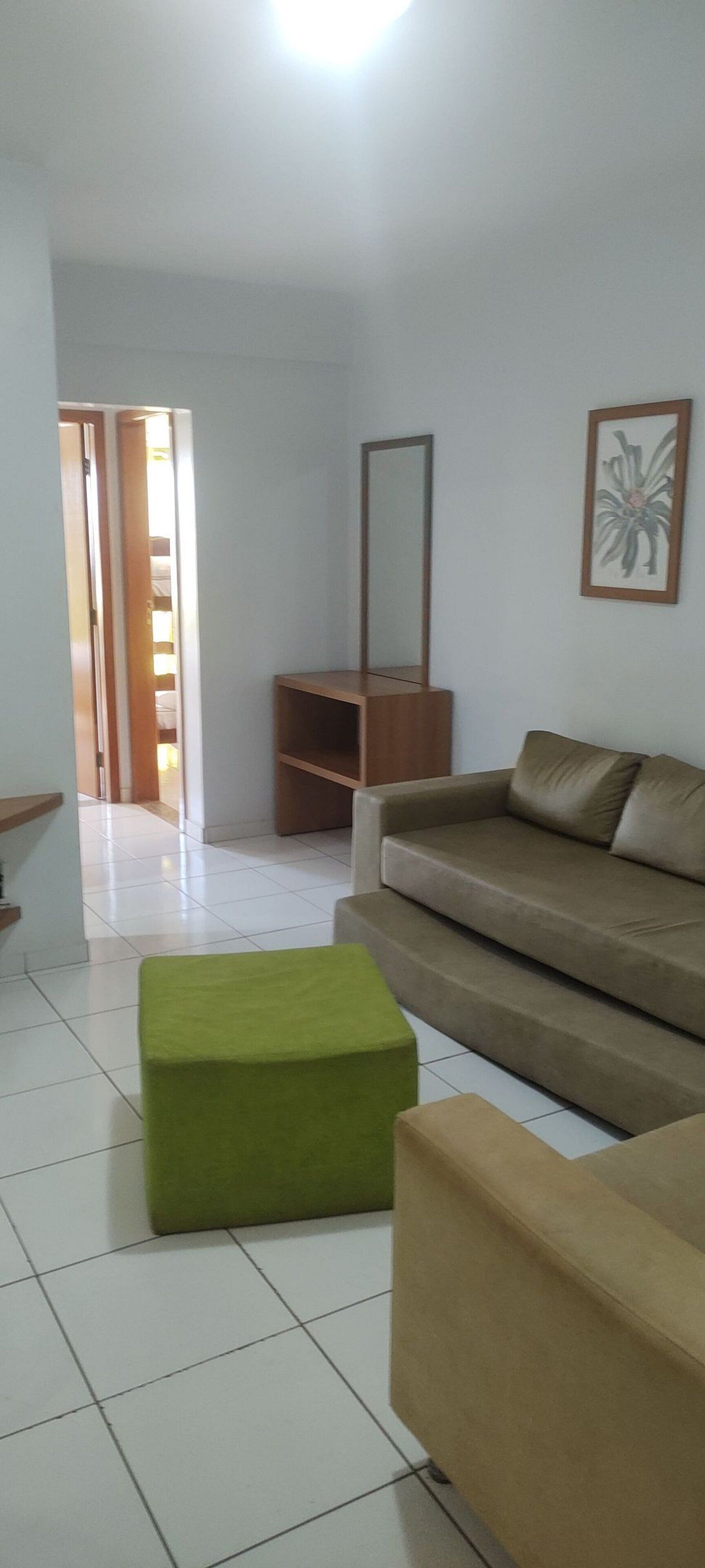 A living room with a sofa, a green ottoman, a wooden cabinet, and a mirror on the wall.