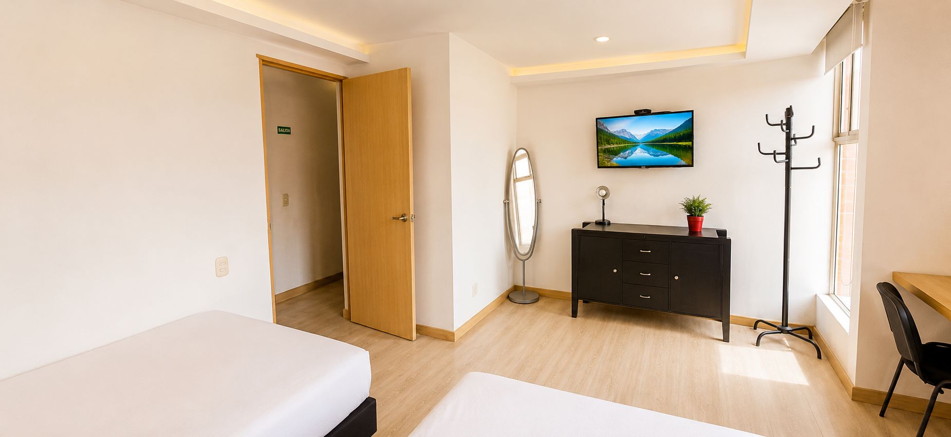 A hotel room with two beds, a TV, a coat rack, and a desk.