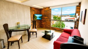 A modern living room with a glass table, red sofa, and a TV mounted on a brick wall. - Your best Laureles home away from home (Medellín)