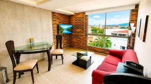 A modern living room with a glass table, red sofa, and a TV mounted on a brick wall.