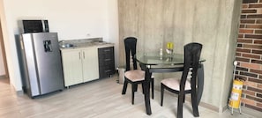 Eine kleine Küche mit Kühlschrank, Spüle und einem Glastisch mit Stühlen.