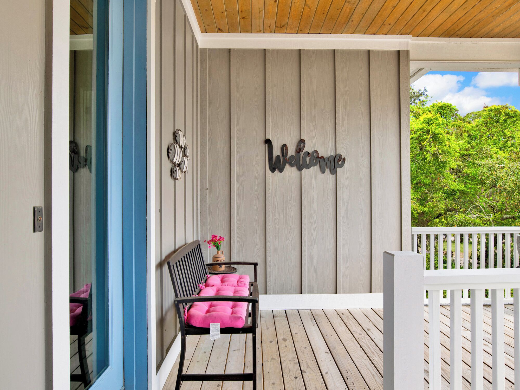 A wooden deck with a white railing, a black chair with a pink cushion, and a 'Welcome' sign on the wall.