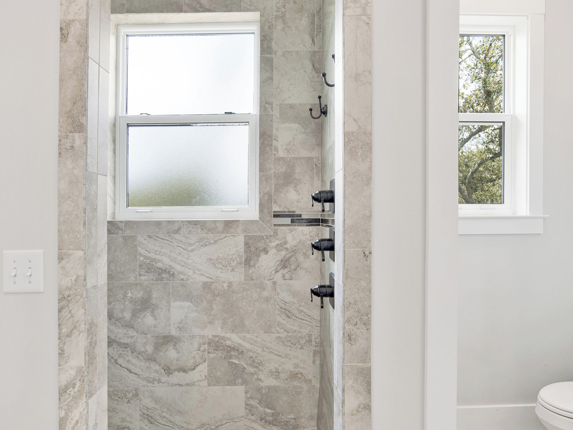 Baño con pared de ducha de piedra, ventana y retrete.