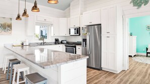 Une cuisine moderne avec des meubles blancs, un réfrigérateur en acier inoxydable, un grand îlot central doté de tabourets et un éclairage suspendu.