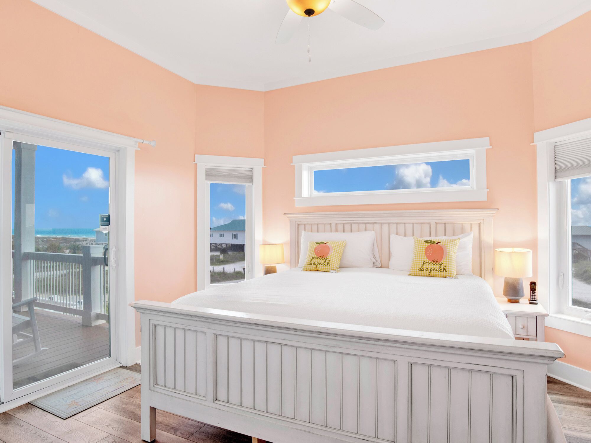 A bedroom with a large bed, two windows with views of the ocean, and a balcony door.