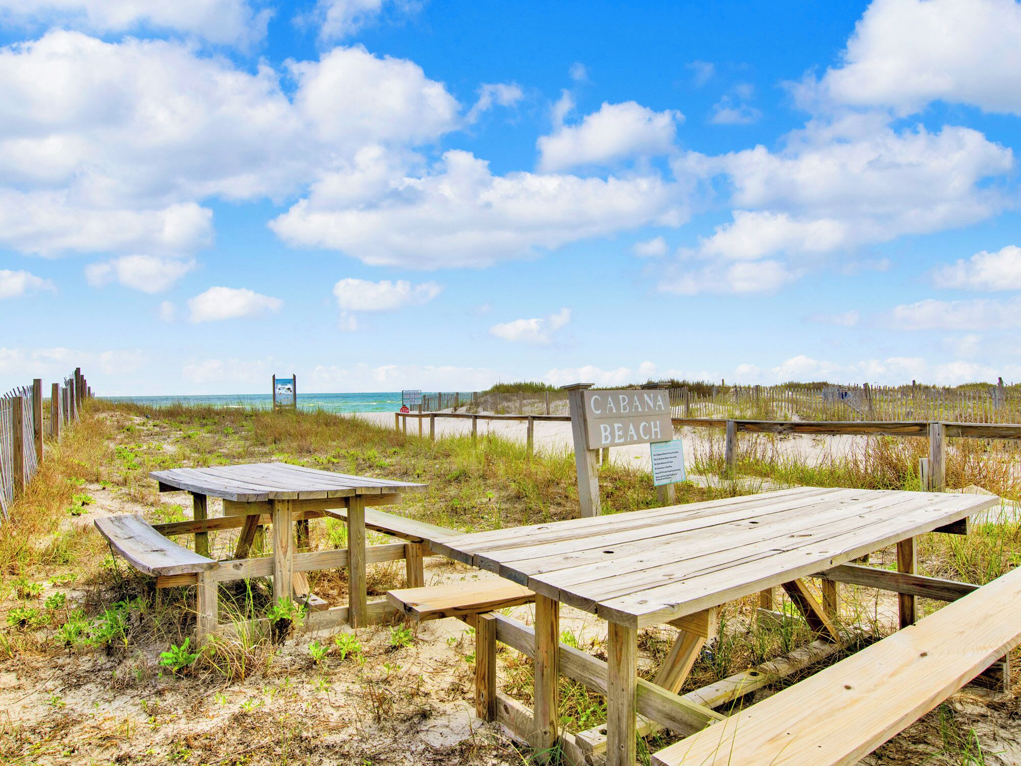 A beach with wooden picnic tables and a sign that reads "CABANA BEACH".