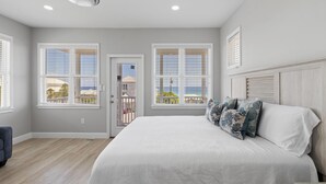 Un dormitorio con una cama grande, dos ventanas con persianas, un ventilador de techo y vistas al exterior.