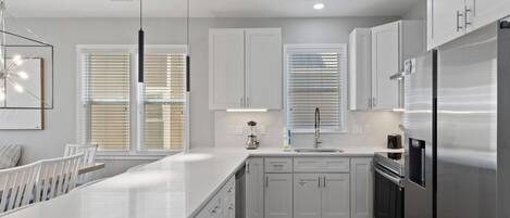 A modern kitchen with white cabinetry, a central island, stainless steel appliances, and pendant lighting.
