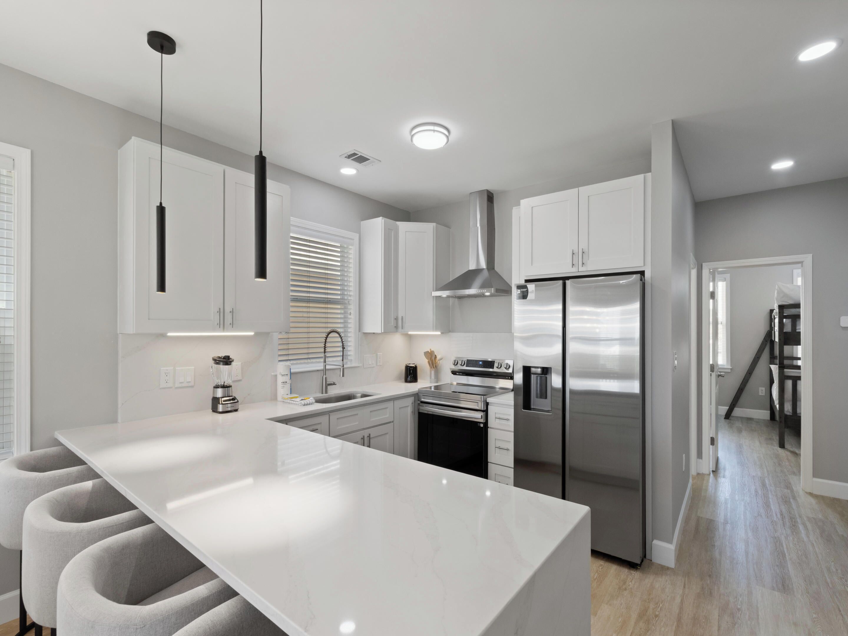 A modern kitchen with a large island, stainless steel appliances, white cabinetry, and pendant lighting.