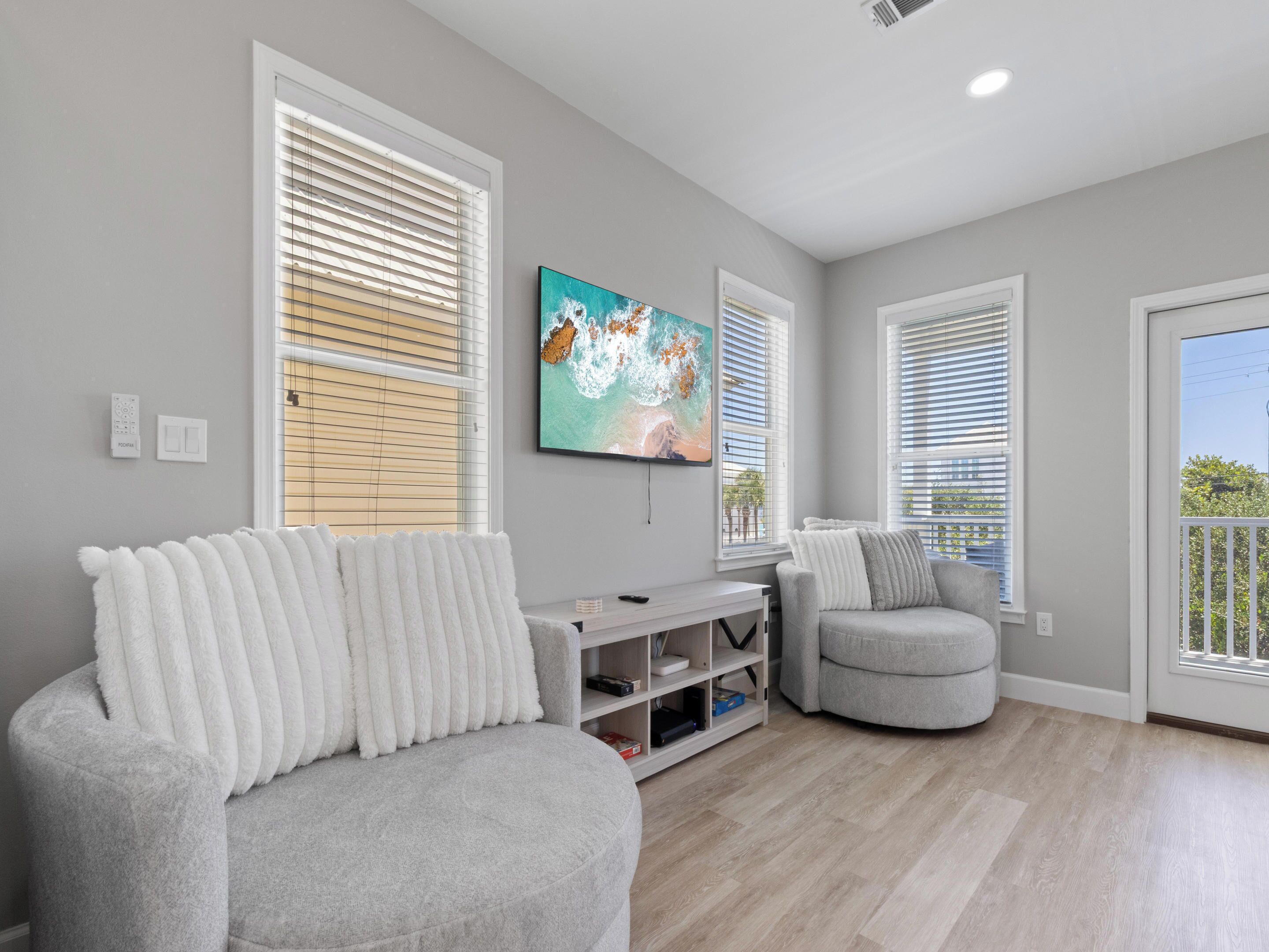 A modern living room with a grey sofa, a grey armchair, and a flat-screen TV mounted on the wall.