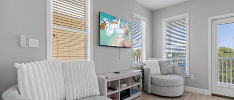 A modern living room with a grey sofa, a grey armchair, and a flat-screen TV mounted on the wall.