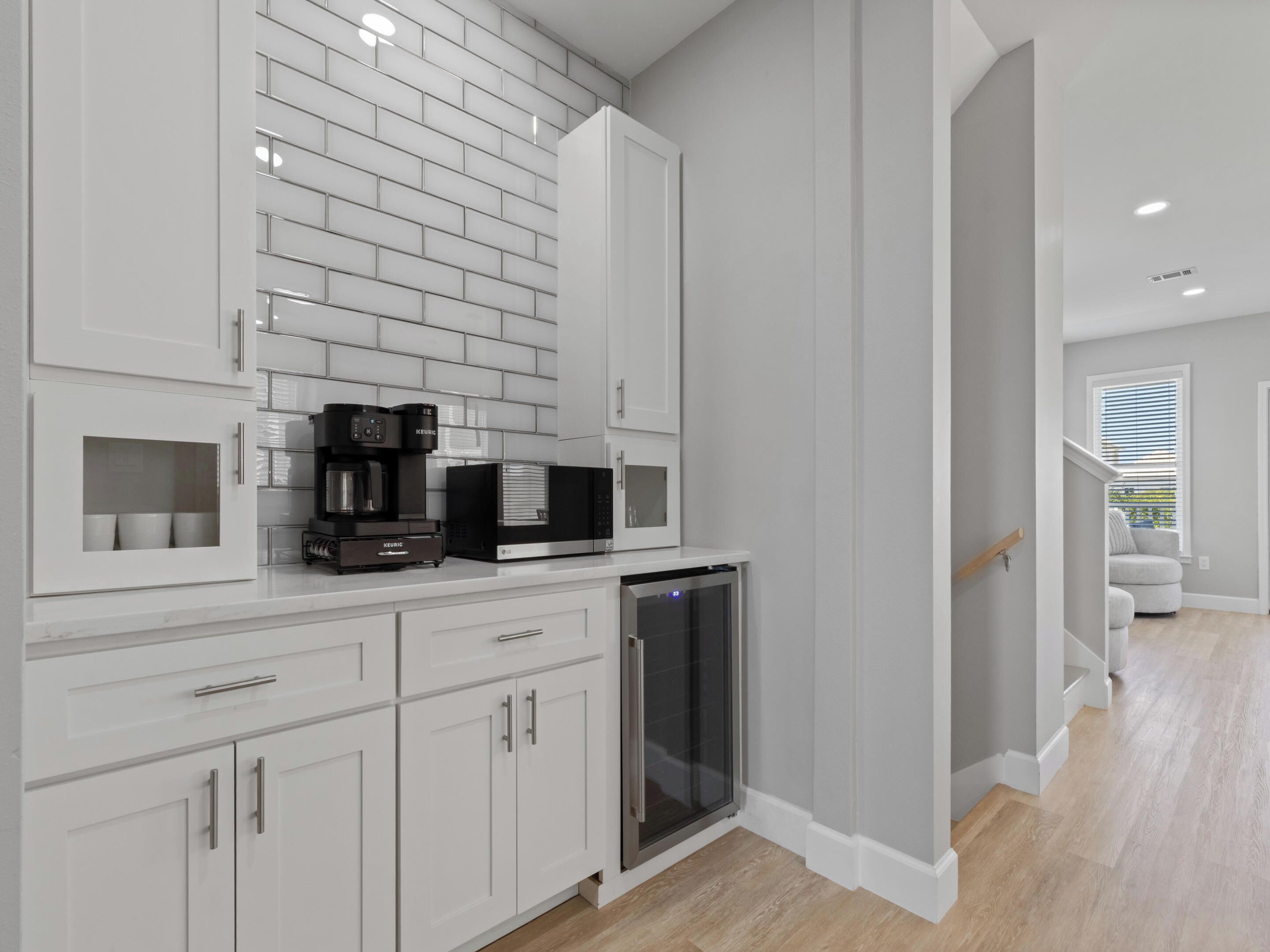 Una cocina moderna con armarios blancos, cafetera, microondas y refrigerador.