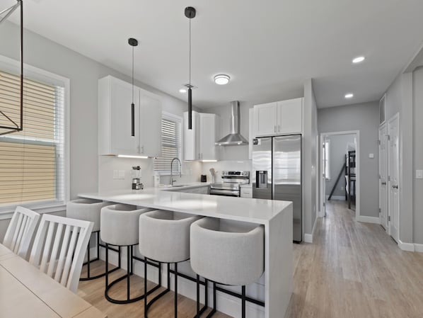A modern kitchen with a central island, bar stools, stainless steel appliances, and a staircase leading to an upper level.