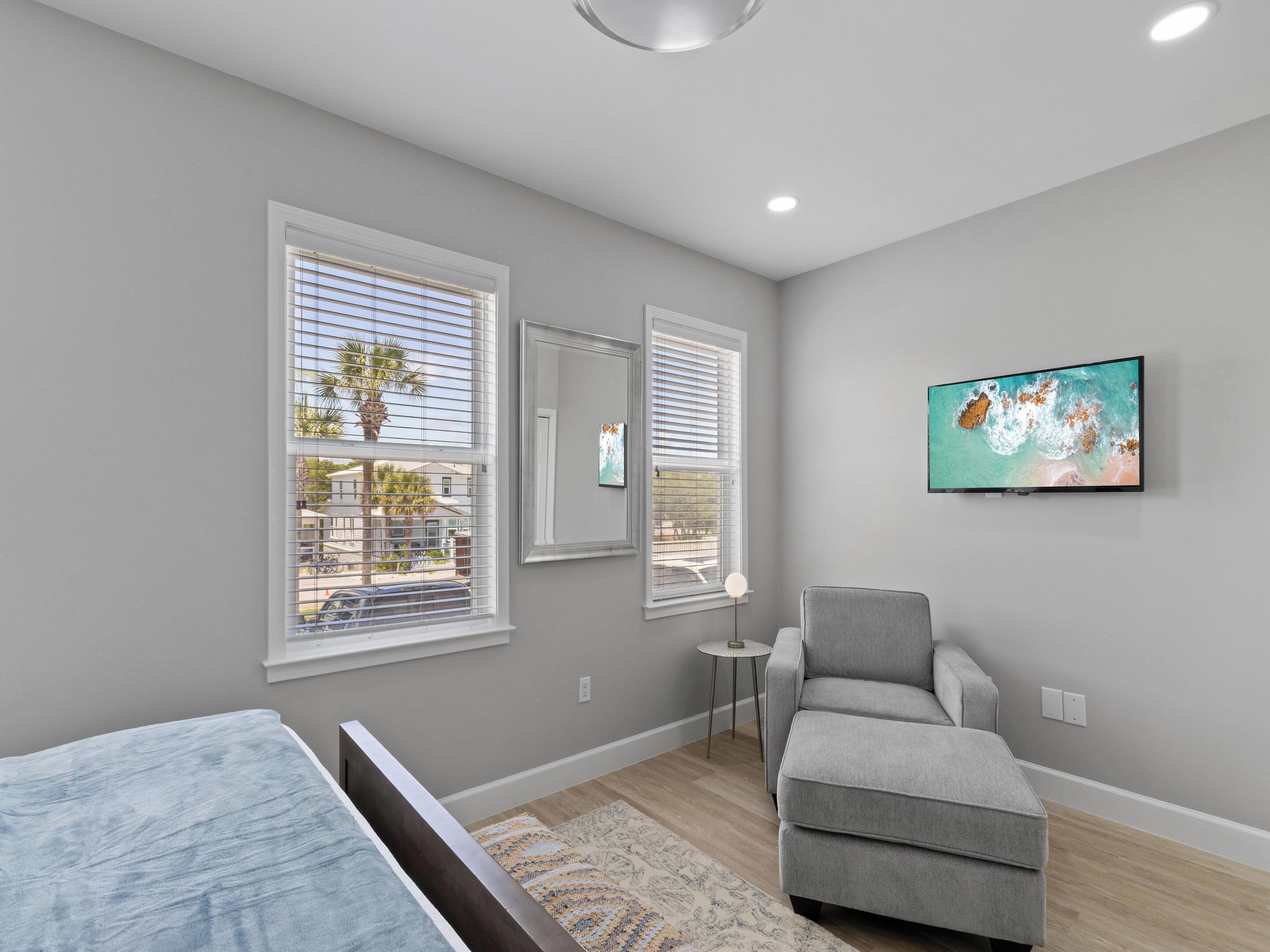 A modern bedroom with a bed, a gray armchair, a small table, and a painting on the wall.
