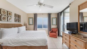 A hotel room with a large bed, a television on a dresser, and a view of the ocean through the window. - Summerchase 1103 (Orange Beach)