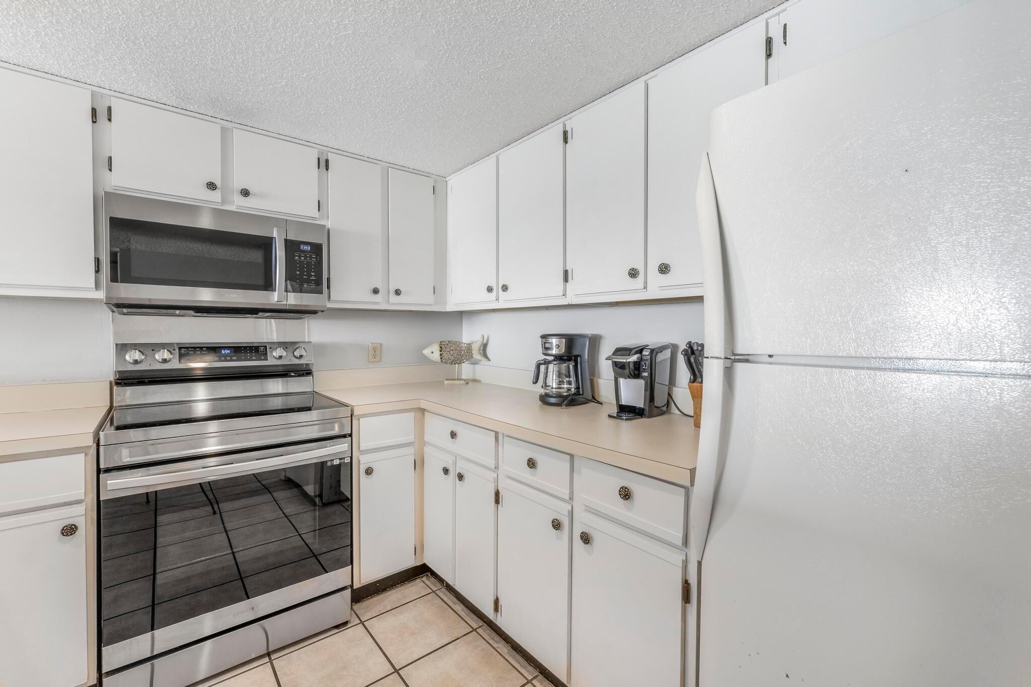 A kitchen with white cabinets, a stainless steel oven, a microwave, a coffee maker, and a refrigerator.