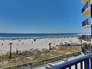 A beach view from a balcony with a clear sky, sandy beach, and a few people. - Sunbird Beach Resort #307 West by Resort Collection (Panama City Beach)