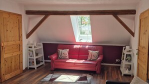 Ein gemütliches Zimmer mit einem roten Ledersofa, Holzbalken, einem Oberlicht und Blick auf Bäume.