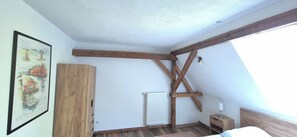 Une chambre avec des poutres apparentes, un radiateur, une table de chevet et un tableau encadré au mur.